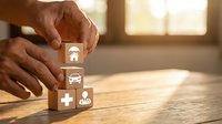 Male hands arranging wooden blocks with insurance icons including umbrella, car, medical cross and family symbols on desk for coverage planning.