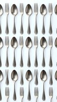 Vintage silver forks and spoons arranged in a repeating flat lay pattern on a white background, tiling into a seamless cutlery backdrop.
