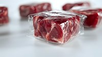 Fresh raw beef cubes wrapped in clear plastic on white surface with selective focus. Meat preparation and packaging concept for food industry and retail.