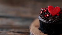 Dark chocolate cupcake topped with rich ganache frosting and red heart decoration on rustic wooden background, romantic dessert for Valentine's Day celebration.
