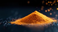 Ground turmeric powder heap illuminated by warm light on dark background with magical bokeh effect and golden particles floating in dramatic atmosphere.