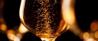 Sparkling champagne or prosecco with golden bubbles rising in a glass against warm bokeh lights, perfect for celebrations and festive occasions.