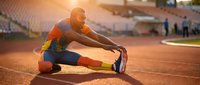 Young Black male athlete stretching on stadium track in colorful sportswear, warming up before race in golden sunlight.
