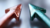 Metallic rose gold and turquoise arrow cursors on reflective surface create modern minimalist composition with selective focus and soft bokeh effect.