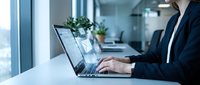 Professional businesswoman working on laptop computer in modern office environment with natural lighting and plants for productivity and success.