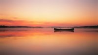 Solitary wooden boat floating on calm water at sunrise with golden and pink sky reflecting on glassy surface, serene landscape for travel and nature projects.