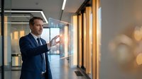 Professional businessman in navy suit presenting strategy in modern corporate office with glass walls and warm lighting for business presentations.