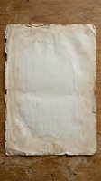 Aged weathered paper sheet with torn edges and stains on rustic wooden background for vintage design projects and antique document mockups.