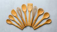 Wooden kitchen utensils set arranged in fan pattern on gray background. Natural bamboo cooking tools for culinary preparation and food service.