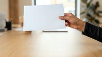 Person of African descent holding blank white card at wooden desk with laptop, suitable for business presentations, marketing mockups, and corporate communications.