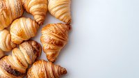 Fresh baked golden croissants scattered on white background, flaky buttery French pastries with crispy layers and various shades of brown, copy space.