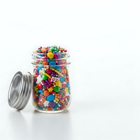 Glass jar filled with colorful candy sprinkles and decorations on white background, isolated for baking and confectionery design projects.