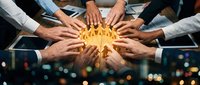 Diverse team of professionals joining hands around glowing lightbulb in circle, symbolizing unity, innovation, collaboration and shared success in business environment.