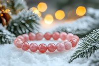 Pink rose quartz crystal bracelet on snowy pine branches with soft golden bokeh lights creating magical winter holiday atmosphere and spiritual ambiance.