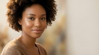 Young African American woman with natural curly hair smiling warmly at camera in soft lighting for lifestyle and portrait photography projects.