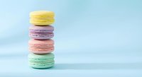 Stack of colorful French macarons in pastel shades including yellow, purple, pink and mint green arranged vertically on soft blue background for bakery menu.