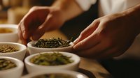 Hands examining loose leaf tea varieties in white ceramic bowls during tea tasting ceremony. Traditional brewing preparation with different green and herbal teas.