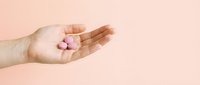 Hand holding pink pills or capsules on neutral beige background, suitable for healthcare, medicine, pharmacy, wellness and pharmaceutical advertising campaigns.
