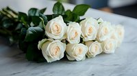 Elegant cream white roses bouquet with fresh green leaves lying on marble surface, soft natural lighting creates romantic mood for wedding and celebration designs.