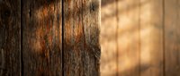 Rustic wooden planks with natural grain texture and warm sunlight casting dappled shadows through leaves creating atmospheric lighting for backgrounds.