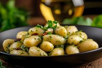 Fresh baby potatoes seasoned with herbs, butter and parsley served in black ceramic bowl, close up view of homemade side dish on rustic wooden table.
