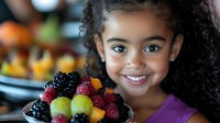Young mixed race girl with curly hair smiling while holding fresh berries and fruits plate, healthy eating lifestyle, natural food concept for children nutrition.
