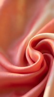 Soft coral pink silk fabric with elegant swirls and smooth texture creating luxurious flowing patterns for fashion and interior design projects.