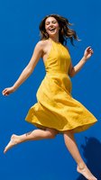 Young woman jumping with joy in bright yellow dress against vibrant blue background expressing happiness freedom and carefree summer energy.