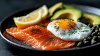 Fresh salmon fillet with sunny side up egg, sliced avocado, capers and lemon on dark plate. Healthy protein-rich breakfast or lunch meal with omega-3 fatty acids.