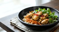 Savory chicken stir-fry with fresh vegetables and herbs served over rice in black bowl on wooden table for healthy meal preparation and cooking content.