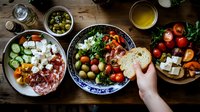 Mediterranean appetizer spread with fresh vegetables, feta cheese, olives, cured meats and bread on rustic wooden table, overhead view of traditional mezze platter.
