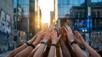 Diverse group of people joining hands together in urban setting during golden hour, symbolizing teamwork, unity, collaboration and community support in city environment.