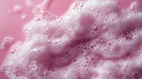 White soap foam and bubbles on pink background, creating abstract texture with soft waves and frothy patterns for cosmetic or cleaning product advertising.