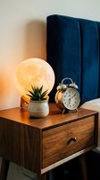 Cozy bedroom nightstand with moon lamp, succulent plant and vintage alarm clock creating warm ambient lighting for modern interior design and home decor.