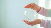Close-up of hands holding a transparent glass sphere against a soft blurred background, symbolizing protection, care, fragility and future vision for business concepts.