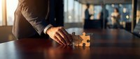 Professional businessman connecting puzzle pieces on wooden desk in modern office environment symbolizing problem solving and strategic planning.