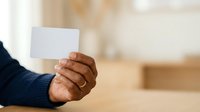 Close-up of male hand holding blank white card indoors, suitable for business presentations, marketing mockups, and promotional campaigns.