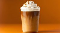 Layered iced coffee drink with whipped cream topping in clear plastic cup against warm brown background, showing distinct coffee and milk gradients.