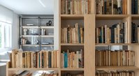 Modern home library with wooden and gray built-in bookshelves displaying organized book collection in bright contemporary living space interior design.