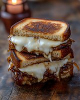 Stacked grilled cheese sandwich with melted mozzarella and caramelized onions on toasted sourdough bread, dripping with golden brown edges on rustic wooden surface.