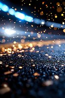 Glowing golden and blue bokeh lights on wet asphalt surface at night create magical atmosphere with sparkling water droplets and blurred background.