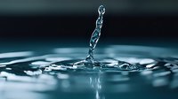 Water drop splash creating a liquid chain formation against dark background with ripples and reflections on water surface in cool blue tones. Macro photography.