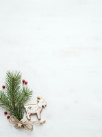 Festive holiday flat lay with evergreen branches, red berries, and decorative wooden reindeer ornament on white wooden surface for seasonal design projects.