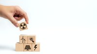Hand placing wooden cube with nuclear symbol on stack showing renewable energy sources including wind, solar and hydroelectric power on white background.