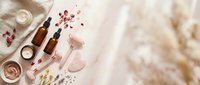 Luxury cosmetics and skincare products arranged flat lay with rose quartz crystals, dried flowers and glass bottles on marble background for beauty and wellness branding.