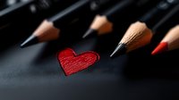 Red heart shape drawn among black graphite pencils on dark background, romantic creative concept for Valentine's Day cards and love messages.