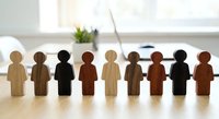 Diverse wooden human figures standing in row on desk representing teamwork, inclusion, unity and workplace diversity in modern office environment.