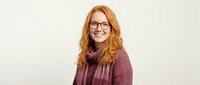 Happy redhead woman with glasses wearing burgundy sweater smiling at camera on neutral background for lifestyle and portrait photography projects.