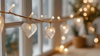 Warm Christmas lights with wooden heart decorations hanging on string create cozy holiday atmosphere in modern home interior with festive tree background.