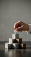 Hand placing white house model on top of stacked wooden blocks in pyramid formation, representing property investment, real estate growth, and business development strategy.